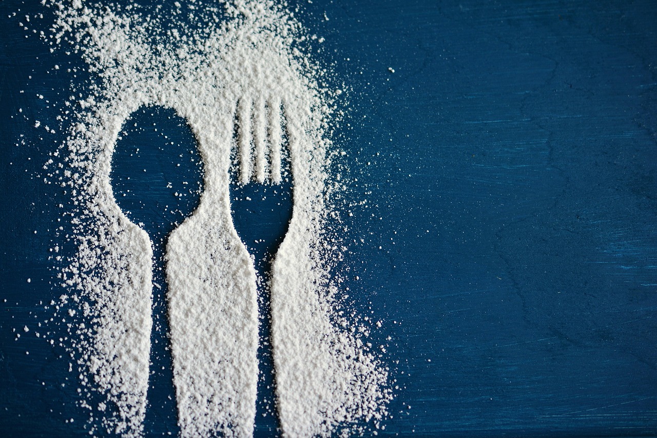 Powdered sugar silhouettes of a spoon and fork on a dark background, representing cutting out added sugar from lunch meals for weight loss