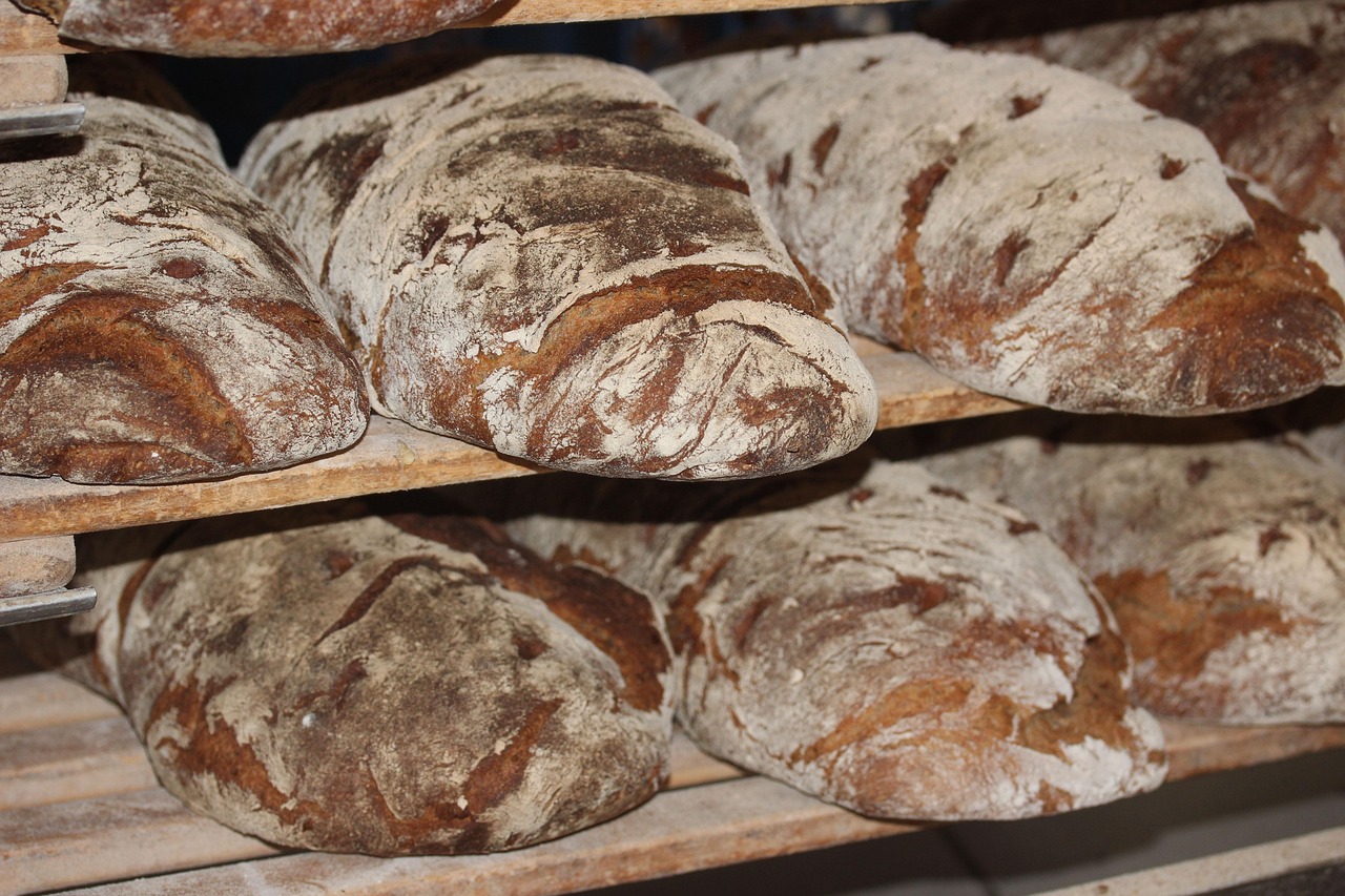 A close-up of several rustic whole-grain and artisan bread loaves resting on a wooden surface, representing healthy sprouted whole-grain bread choices for managing blood pressure