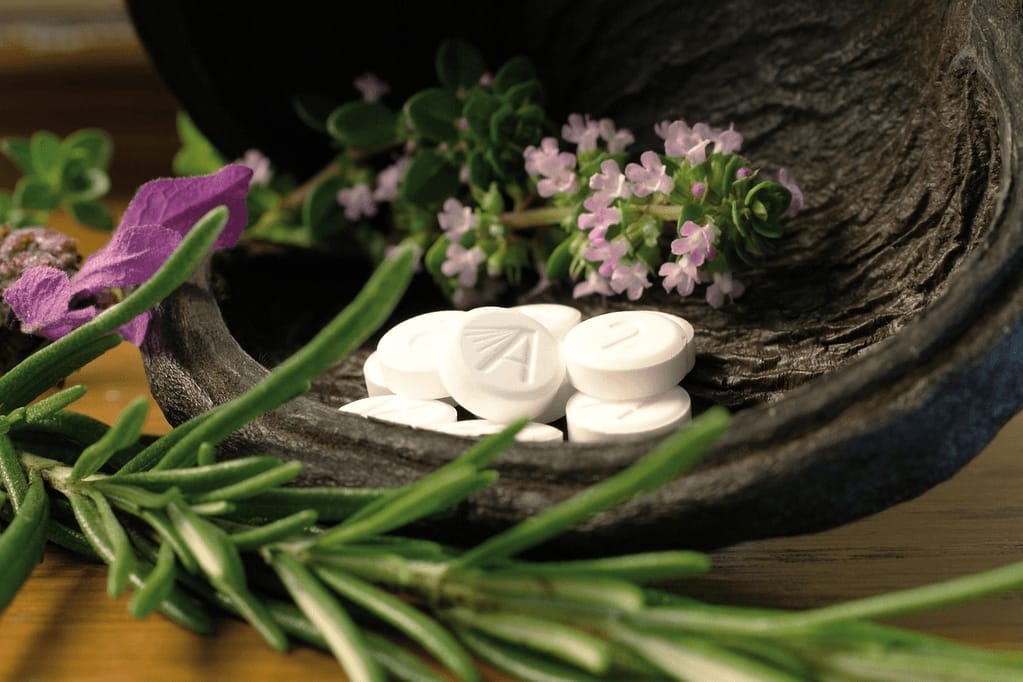 A collection of white pills alongside natural herbs and flowers on a wooden surface, representing both pharmaceutical and natural approaches to GLP-1 alternatives for weight loss.