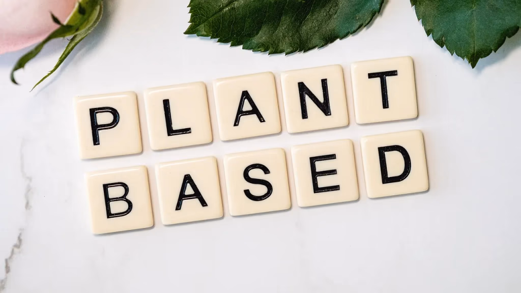 Scrabble tiles spelling out PLANT BASED on a green surface, representing plant-based eating and nutrition