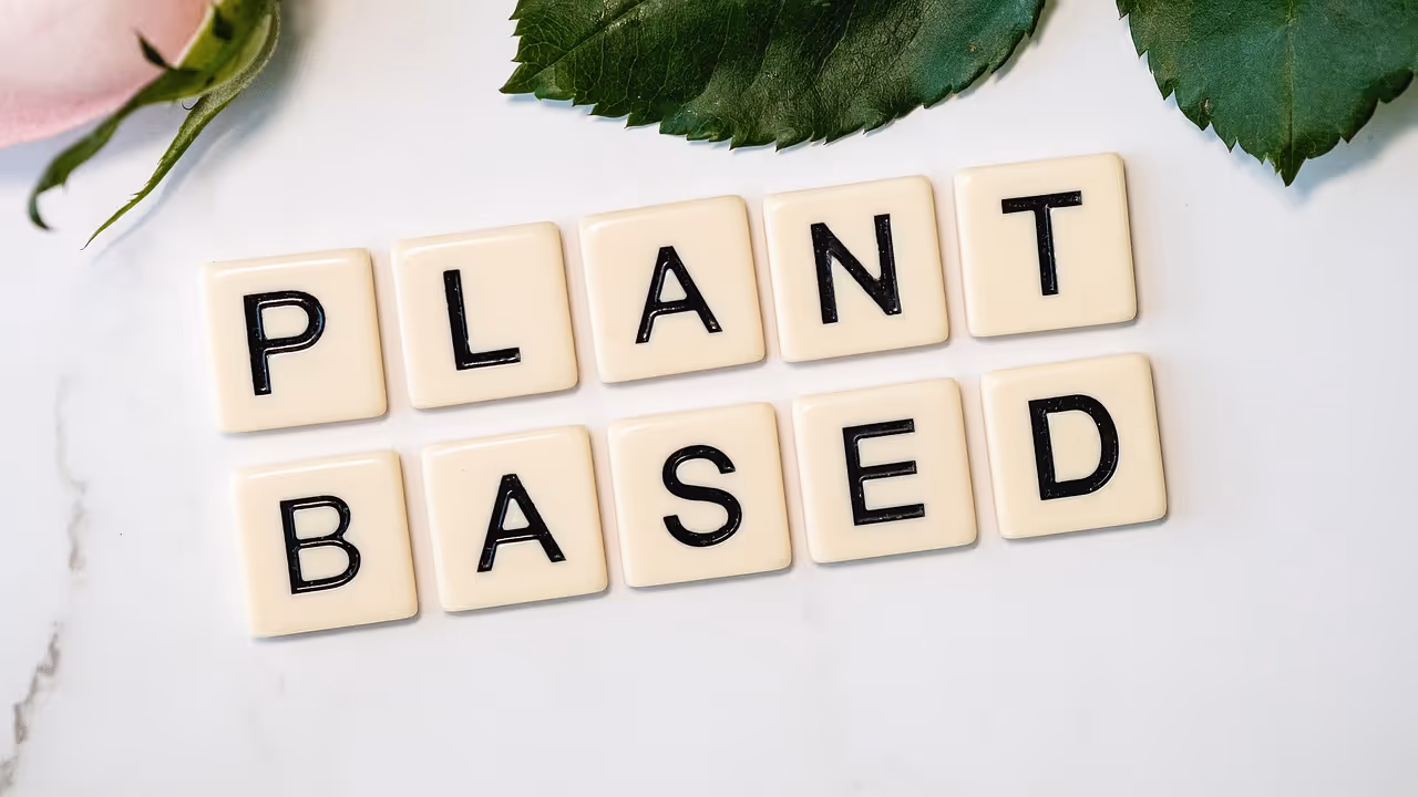 Scrabble tiles spelling out PLANT BASED on a green surface, representing plant-based eating and nutrition