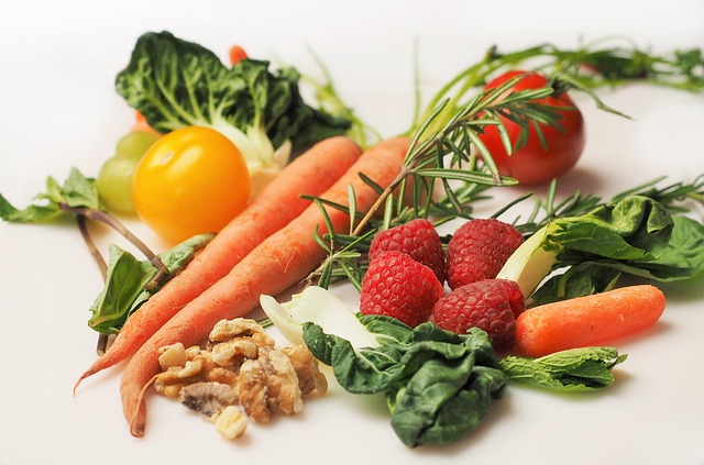 Assortment of fresh colorful vegetables and fruits including carrots, tomatoes, raspberries, and leafy greens arranged on a table — heart-healthy foods for lowering blood pressure naturally with the DASH diet