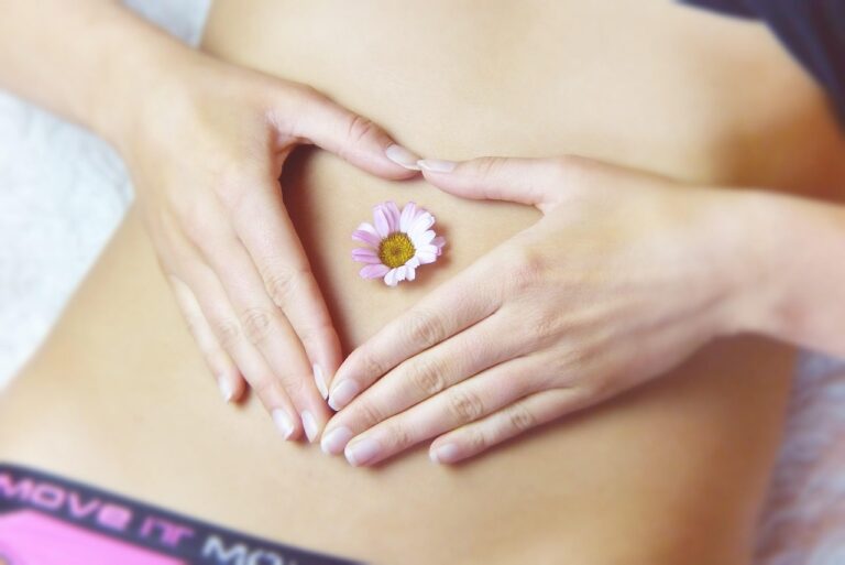Woman in white shirt holding her stomach with a concerned expression, representing the experience of PCOS belly - a combination of hormonal bloating and visceral fat common in polycystic ovary syndrome
