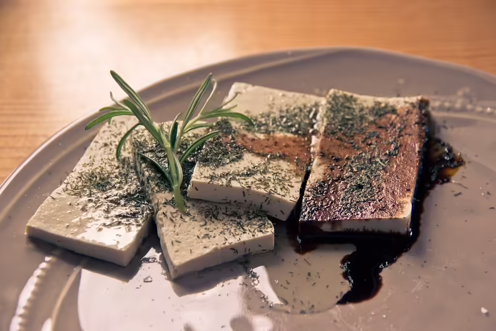 A block of fresh tofu on a plate with green leafy vegetables, representing a whole food plant-based protein option with minimal processing