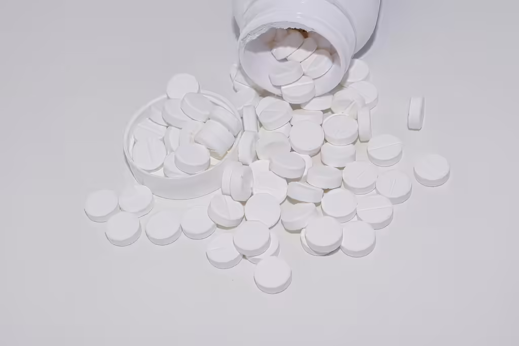 White supplement pills and tablets spilling out of a glass bottle, representing sleep aids like magnesium and melatonin supplements for better sleep quality