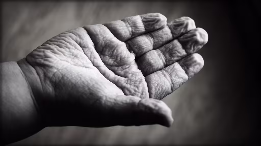 Close-up of two hands touching — one wrinkled aging hand and one younger hand — representing solo aging, connection, and the need for supportive care networks in later life.
