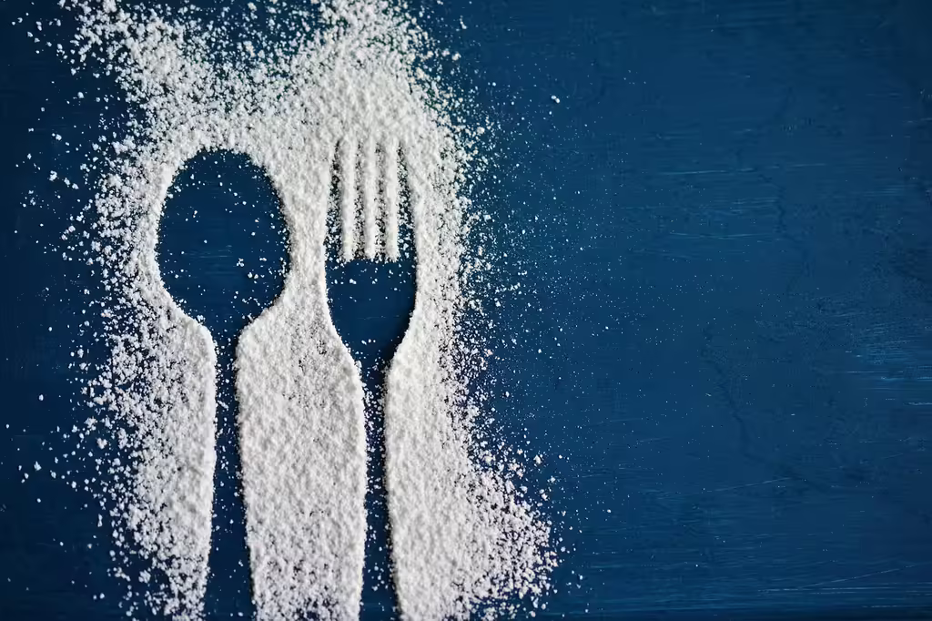 Powdered sugar silhouettes of a spoon and fork on a dark background, representing cutting out added sugar from lunch meals for weight loss