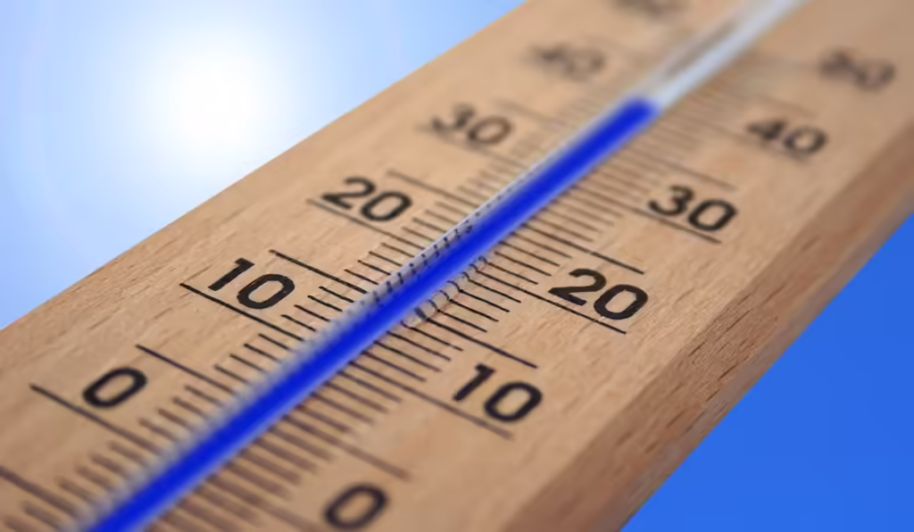 Outdoor thermometer showing high temperature against a bright sunny sky, representing extreme heat and heat wave conditions